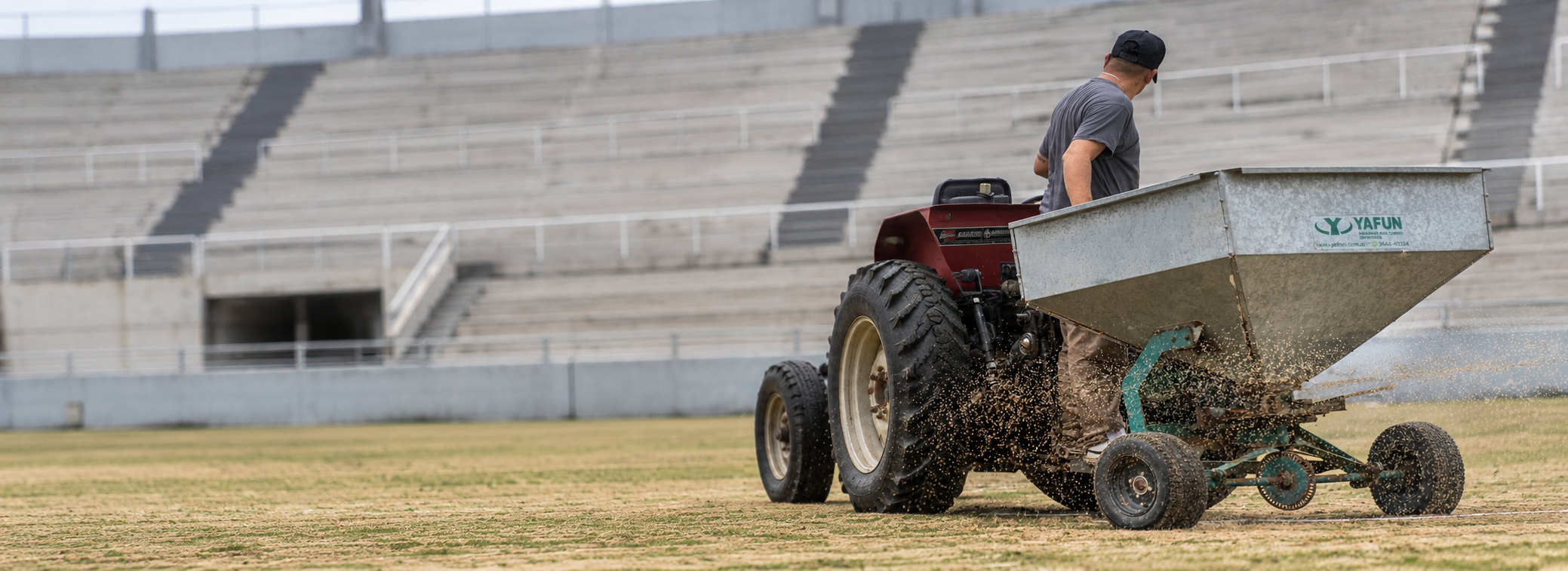 Operario con tractor y arenadora Yafun distribuyendo material sobre el césped de un estadio