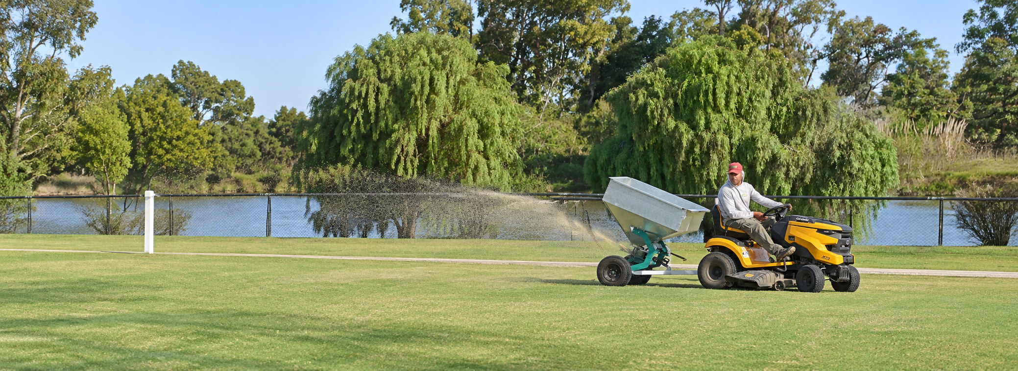 Operario con tractor de jardín y arenadora Yafun distribuyendo material sobre un campo de césped
